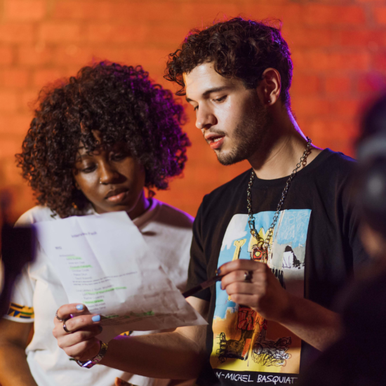 2 young people, one black woman, one white guy looking at a sheet of paper.